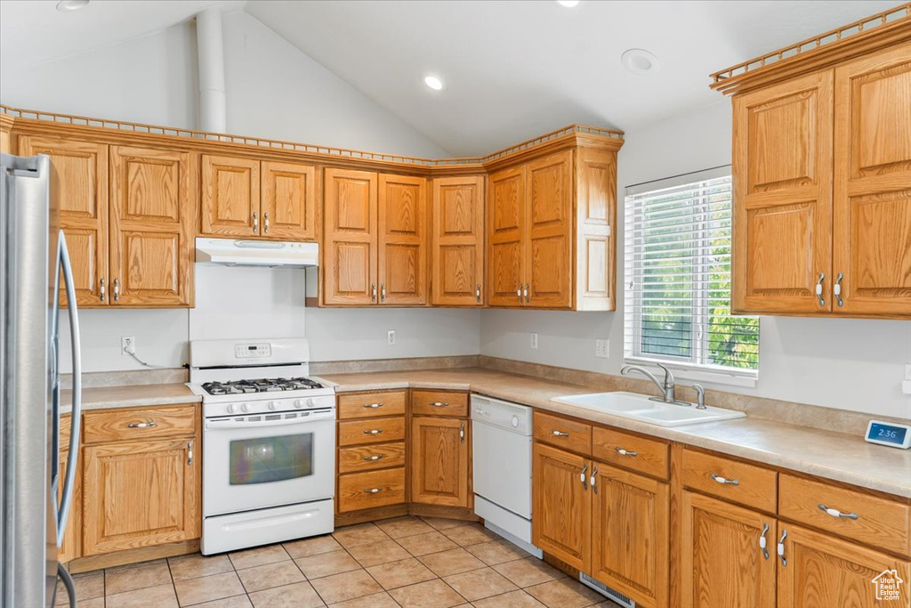 Kitchen with white appliances, under cabinet range hood, a sink, light tile patterned floors, and vaulted ceiling