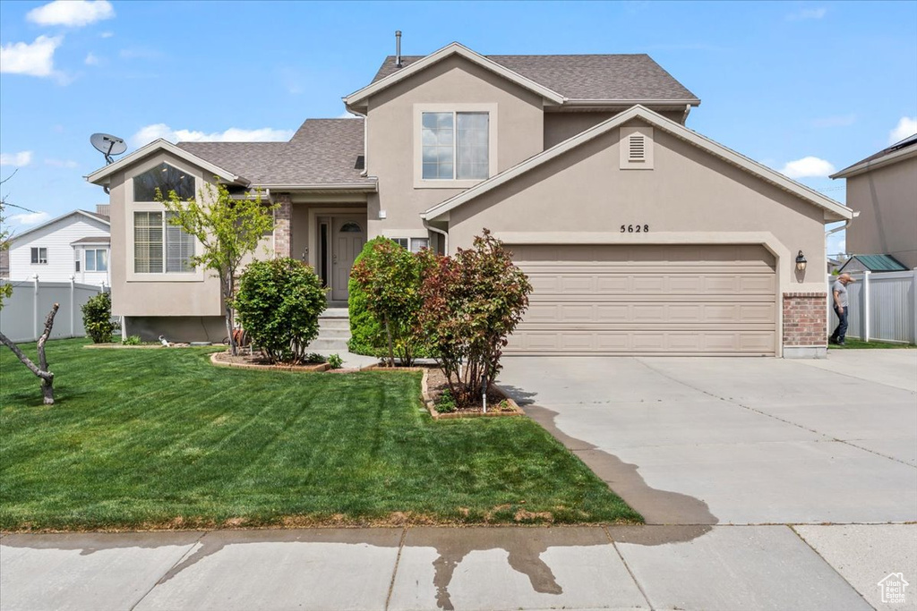 View of front facade featuring a front lawn, fence, stucco siding, a shingled roof, and driveway