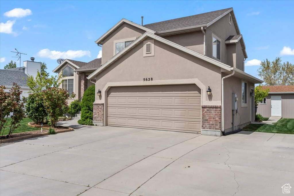 Traditional-style house featuring brick siding, an attached garage, driveway, and stucco siding