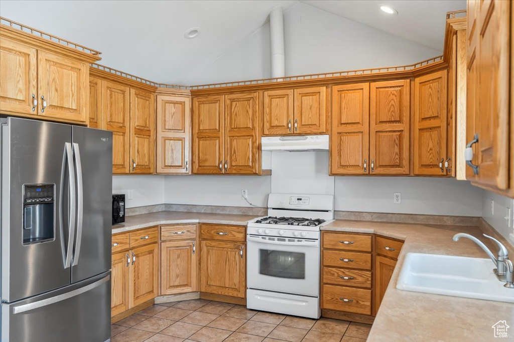 Kitchen with white gas range, stainless steel refrigerator with ice dispenser, light countertops, under cabinet range hood, and a sink