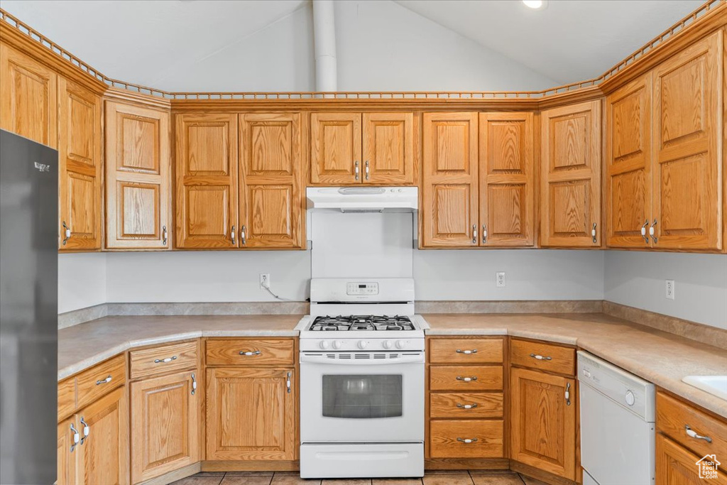 Kitchen with white appliances, light countertops, under cabinet range hood, brown cabinets, and vaulted ceiling