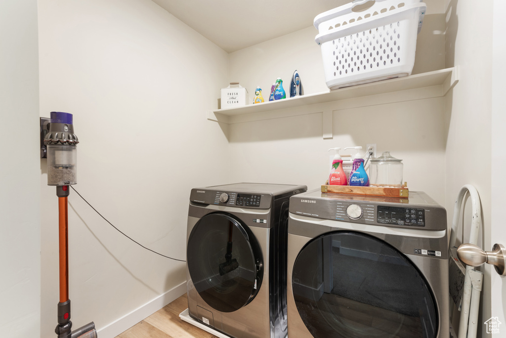 Clothes washing area with washing machine and clothes dryer, laundry area, baseboards, and wood finished floors