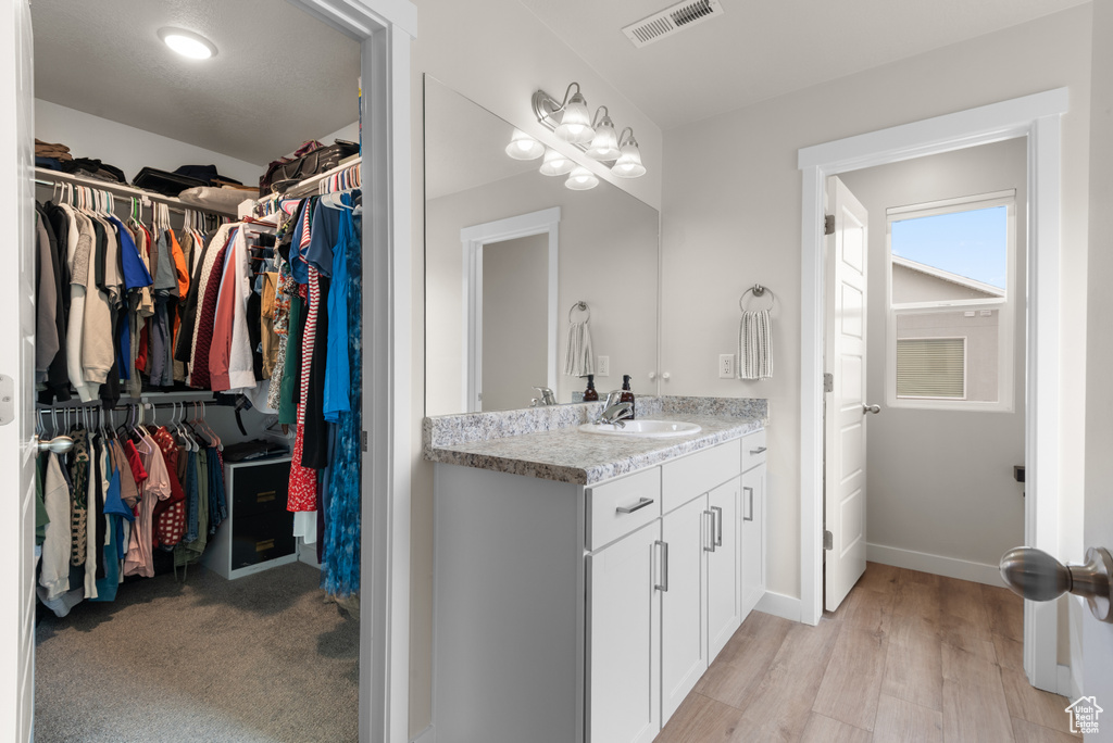Bathroom with a walk in closet, vanity, baseboards, wood finished floors, and visible vents
