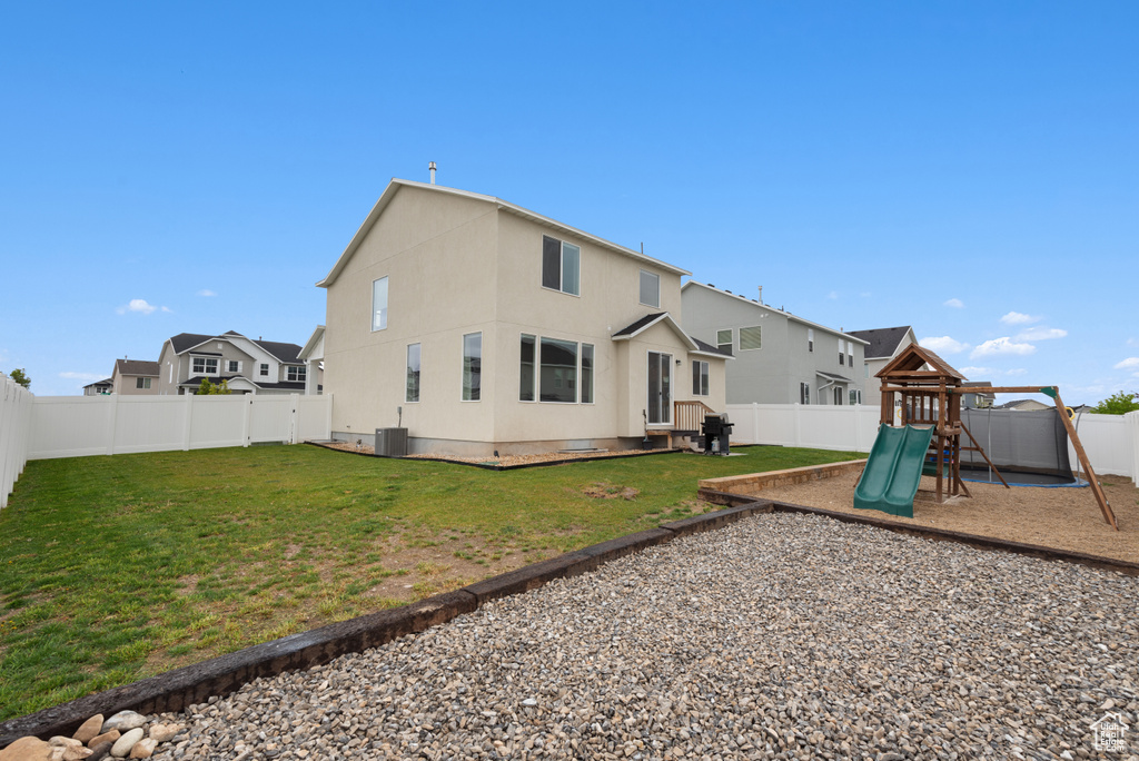 Back of house with a fenced backyard, a playground, central air condition unit, and a yard