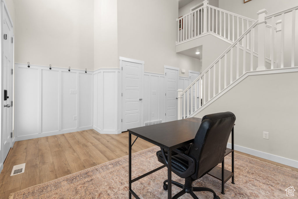 Home office featuring visible vents, a towering ceiling, a decorative wall, wood finished floors, and a wainscoted wall
