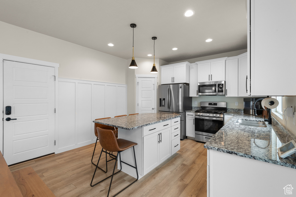 Kitchen with light wood-type flooring, white cabinetry, a breakfast bar area, and stainless steel appliances