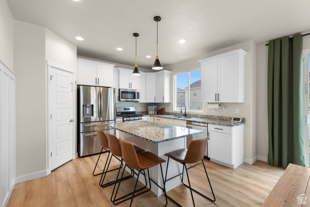 Kitchen with appliances with stainless steel finishes, a sink, light wood-style floors, white cabinetry, and a kitchen island