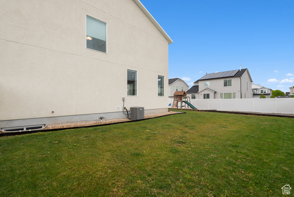 Rear view of property featuring a lawn, central AC unit, fence, a playground, and stucco siding