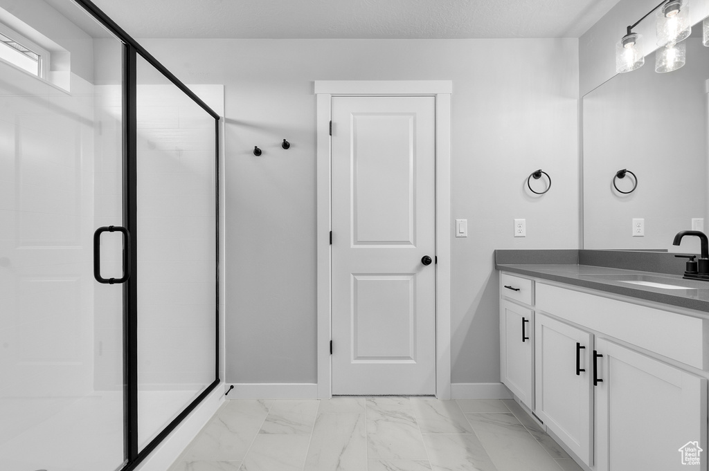 Full bath featuring vanity, a shower stall, baseboards, and marble look tiles