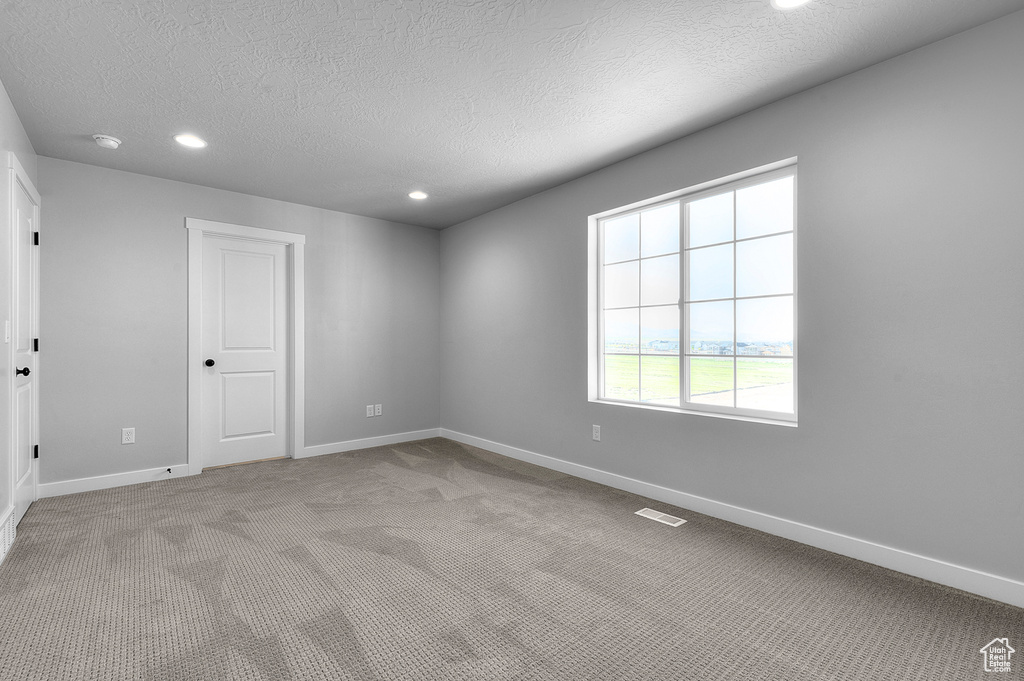 Spare room featuring light colored carpet, a textured ceiling, baseboards, and recessed lighting