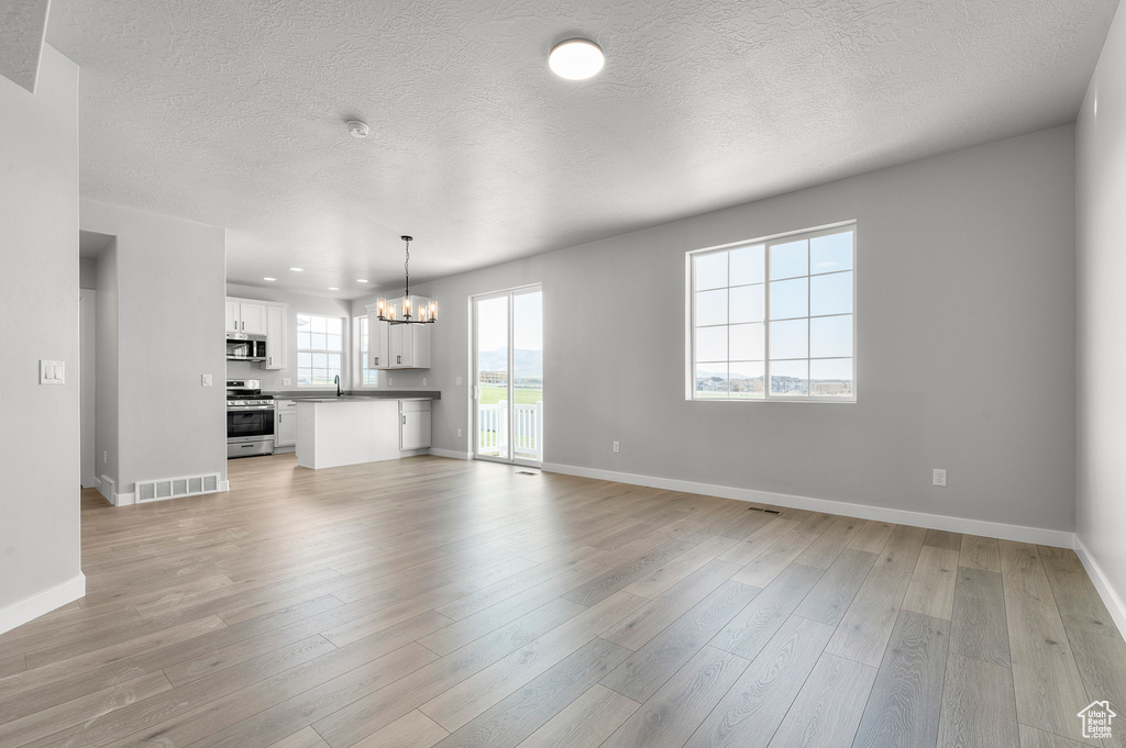 Unfurnished living room with a chandelier, a sink, light wood finished floors, baseboards, and a textured ceiling