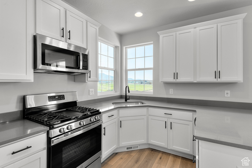 Kitchen featuring appliances with stainless steel finishes, a sink, recessed lighting, white cabinets, and light wood finished floors