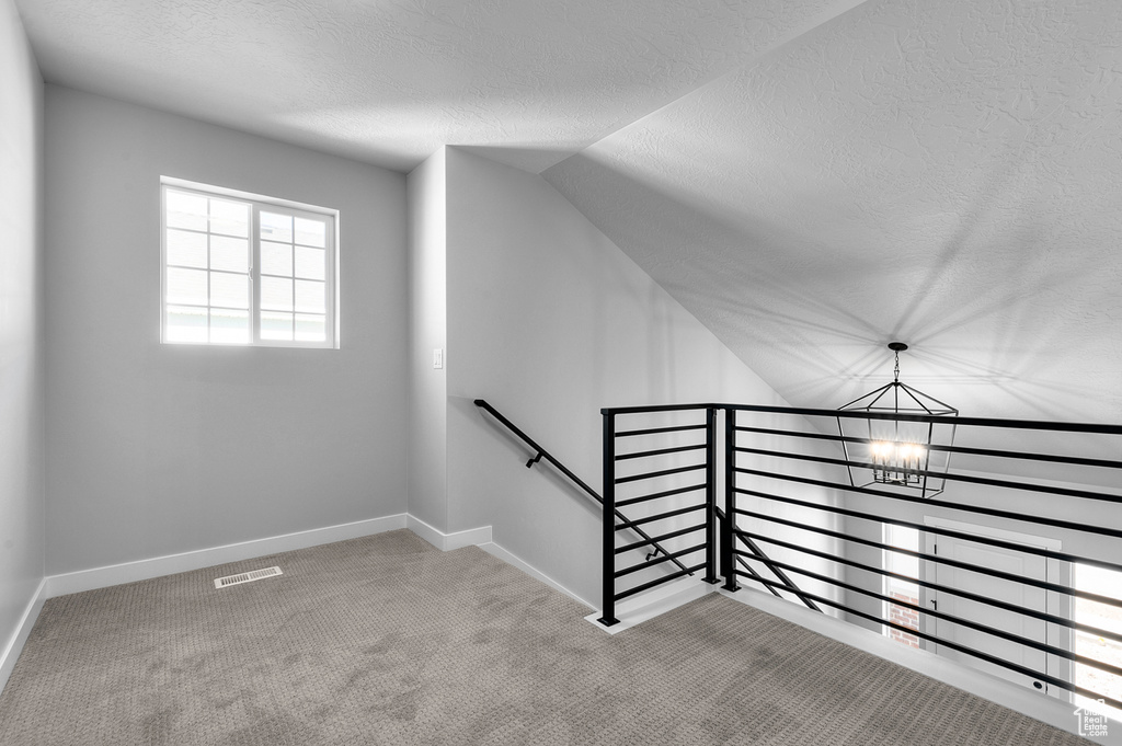 Staircase featuring a chandelier, a textured ceiling, carpet flooring, lofted ceiling, and baseboards