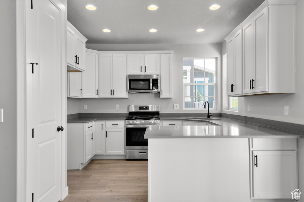 Kitchen with appliances with stainless steel finishes, a sink, recessed lighting, a peninsula, and white cabinets