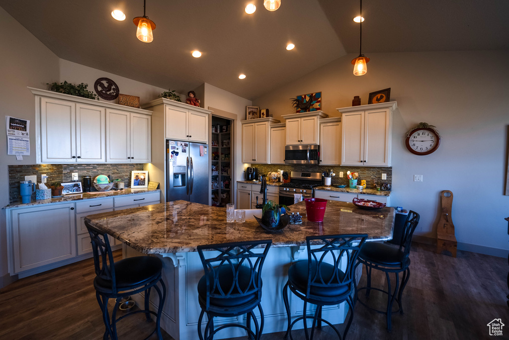 Kitchen with appliances with stainless steel finishes, backsplash, vaulted ceiling, and dark wood-style flooring