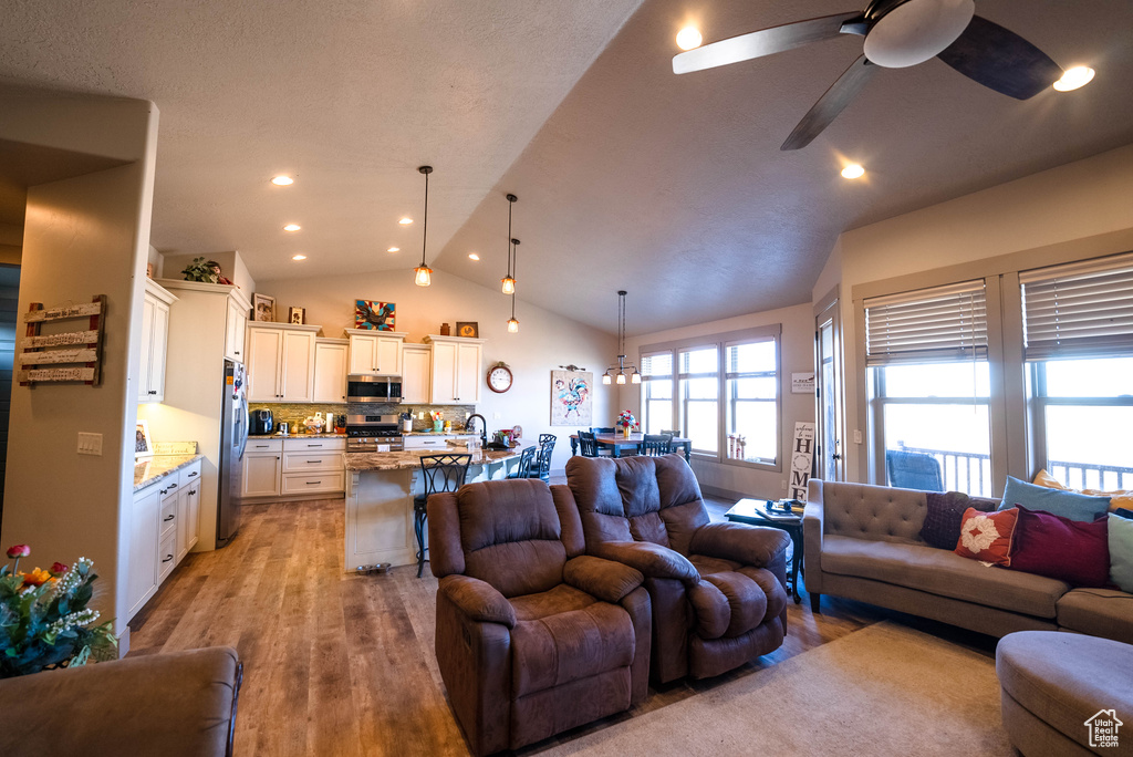 Living area with a ceiling fan, vaulted ceiling, recessed lighting, and light wood-style flooring