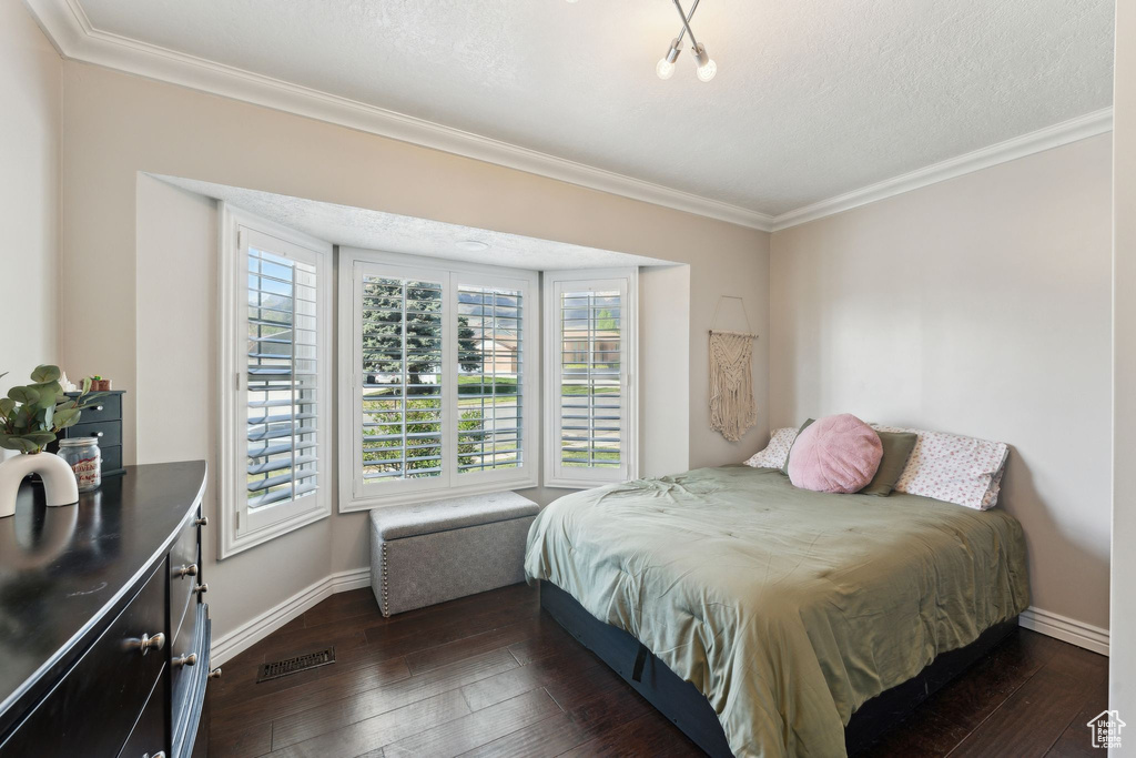 Bedroom with a textured ceiling, baseboards, dark wood-type flooring, visible vents, and ornamental molding