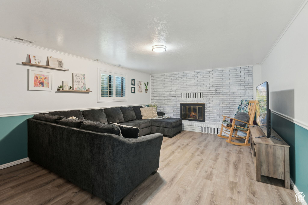 Living room with baseboards, a brick fireplace, wood finished floors, and visible vents