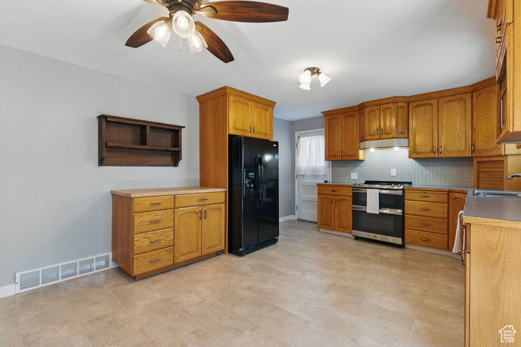 Kitchen with visible vents, black refrigerator with ice dispenser, under cabinet range hood, range with two ovens, and a sink