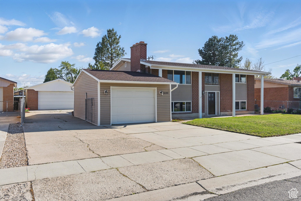 Bi-level home with a chimney, an attached garage, brick siding, and a front yard