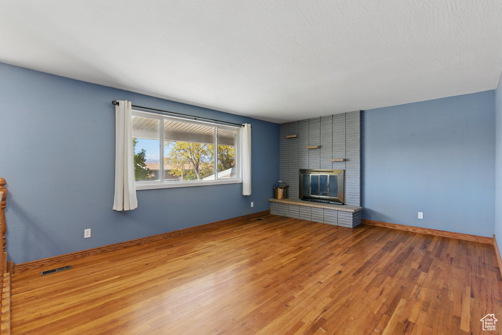 Unfurnished living room featuring visible vents, baseboards, a brick fireplace, and wood finished floors