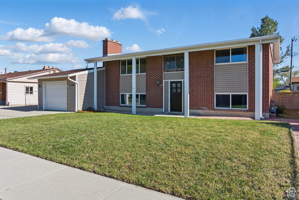 Raised ranch with an attached garage, brick siding, a front yard, a chimney, and concrete driveway