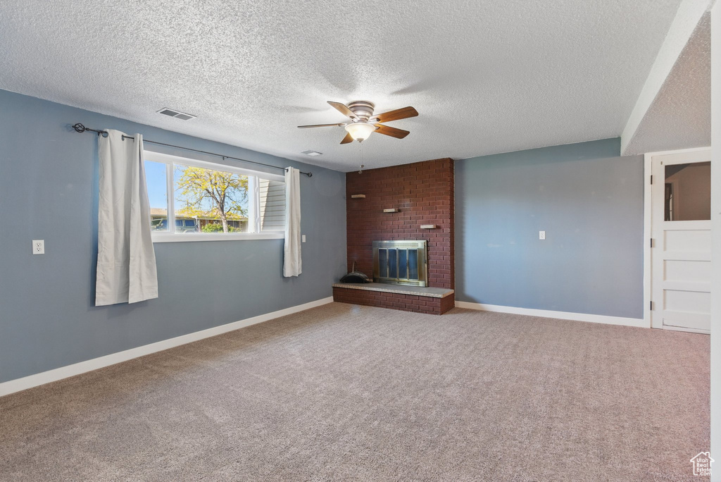 Unfurnished living room with a ceiling fan, a textured ceiling, visible vents, a fireplace, and carpet flooring