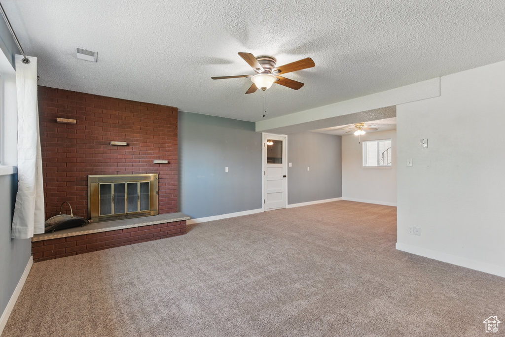 Unfurnished living room featuring a fireplace, baseboards, ceiling fan, a textured ceiling, and carpet