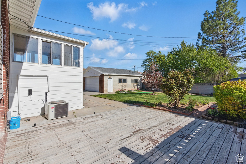 Wooden terrace with an outdoor structure, a lawn, central air condition unit, and fence