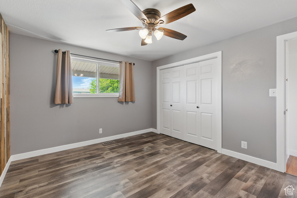 Unfurnished bedroom featuring ceiling fan, dark wood finished floors, baseboards, visible vents, and a closet