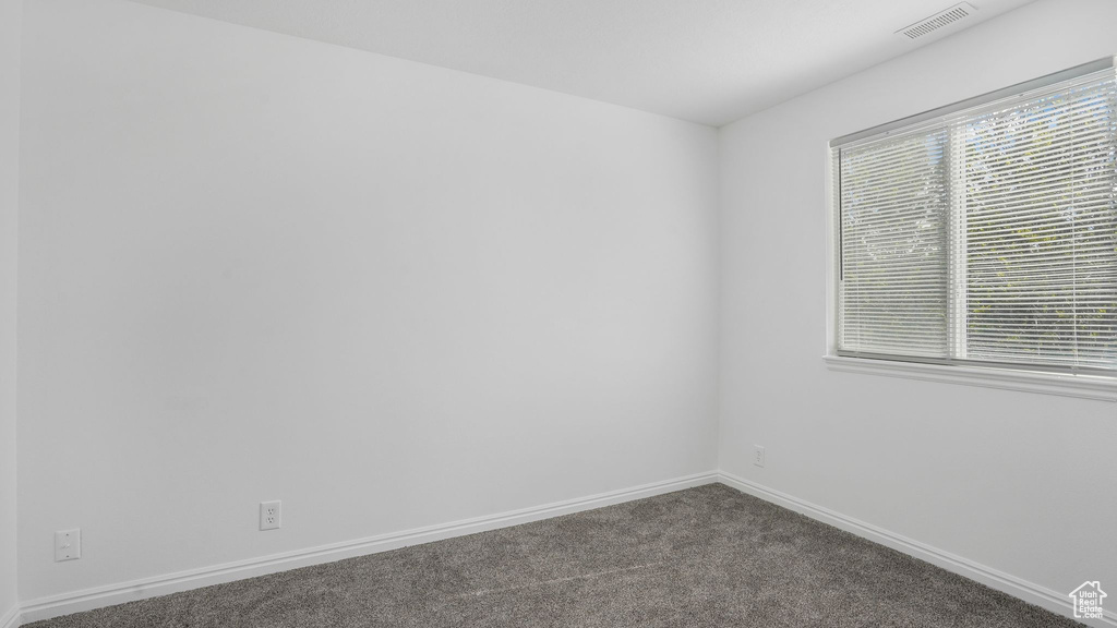 Empty room with baseboards, dark colored carpet, and visible vents