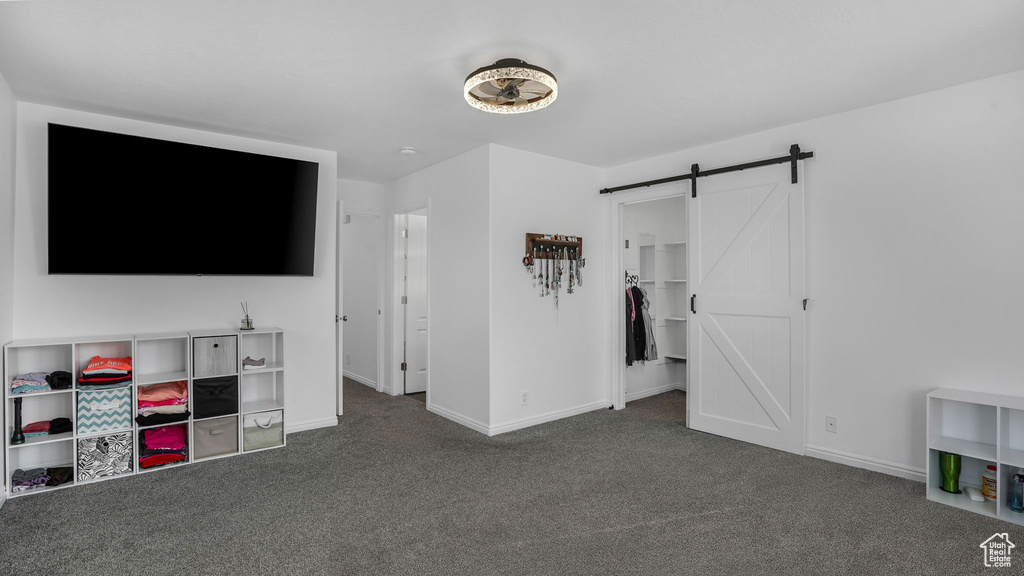 Unfurnished bedroom with baseboards, dark carpet, a barn door, and a spacious closet