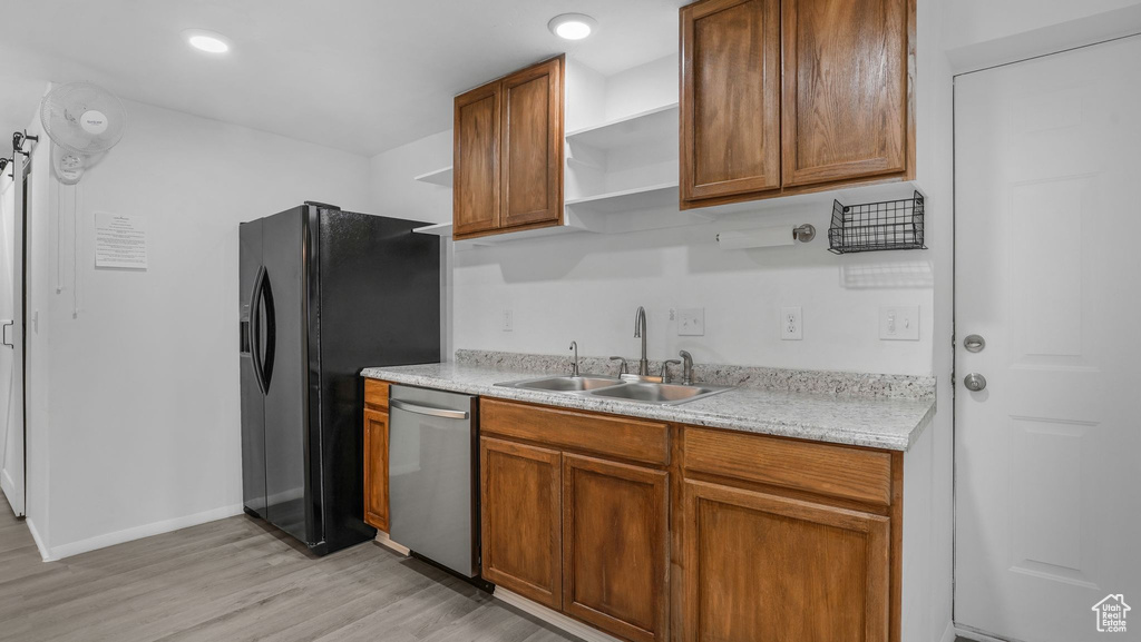Kitchen with open shelves, stainless steel dishwasher, a sink, light wood finished floors, and black fridge