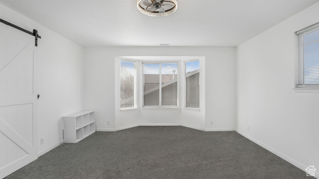 Spare room with dark carpet, a barn door, and baseboards