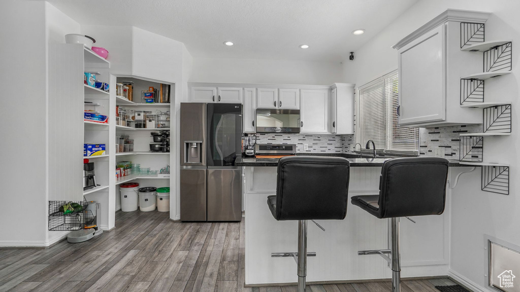 Kitchen with stainless steel refrigerator with ice dispenser, open shelves, dark countertops, and white cabinetry