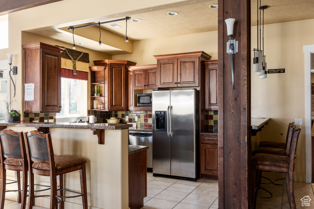 Kitchen featuring a peninsula, dark countertops, a kitchen breakfast bar, stainless steel refrigerator with ice dispenser, and built in microwave
