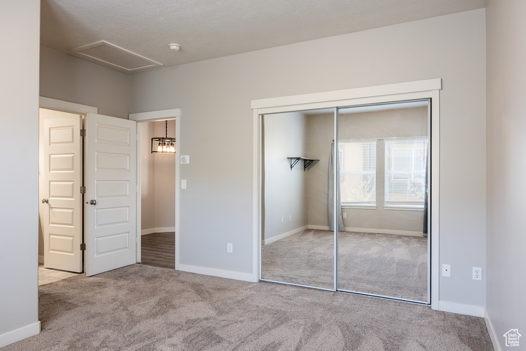 Unfurnished bedroom featuring carpet flooring, baseboards, attic access, and a closet