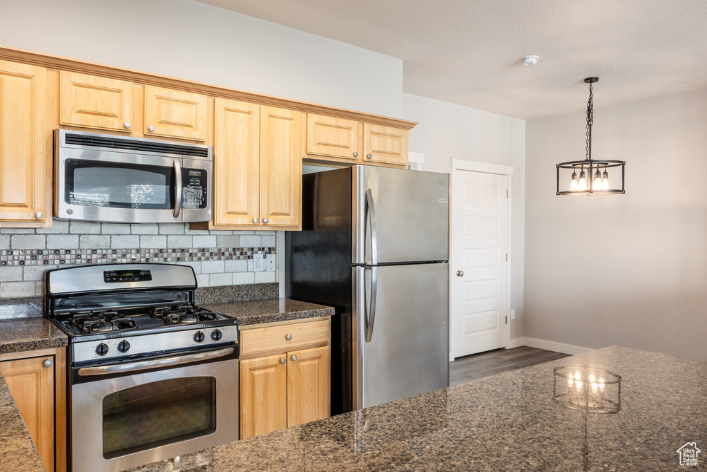 Kitchen featuring appliances with stainless steel finishes, a chandelier, baseboards, decorative backsplash, and wood finished floors
