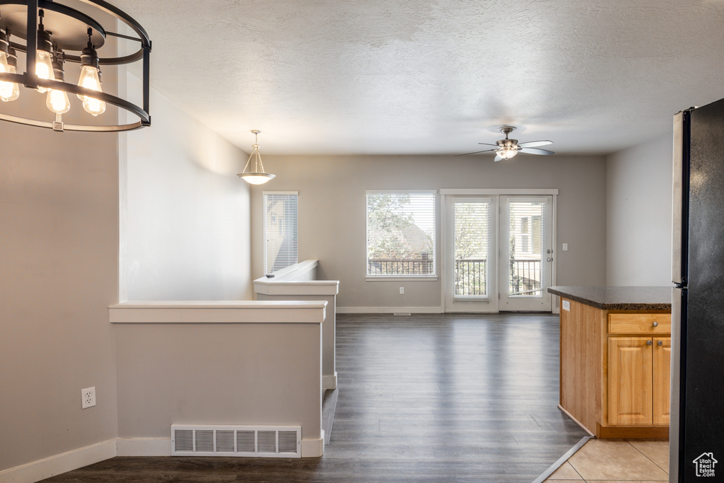 Unfurnished dining area featuring a textured ceiling, ceiling fan with notable chandelier, baseboards, wood finished floors, and visible vents