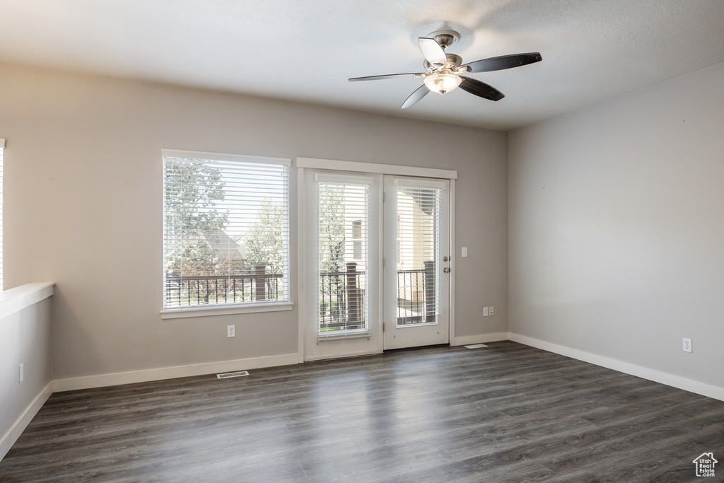 Empty room featuring a healthy amount of sunlight, ceiling fan, and dark wood-type flooring