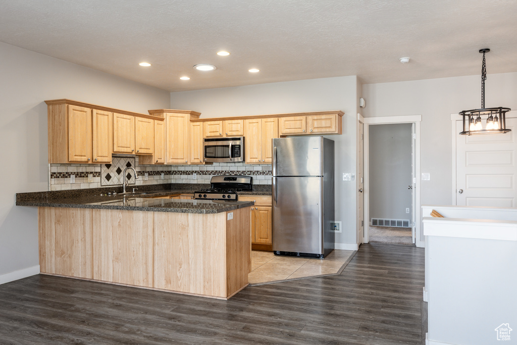 Kitchen with visible vents, a peninsula, light brown cabinetry, wood finished floors, and appliances with stainless steel finishes