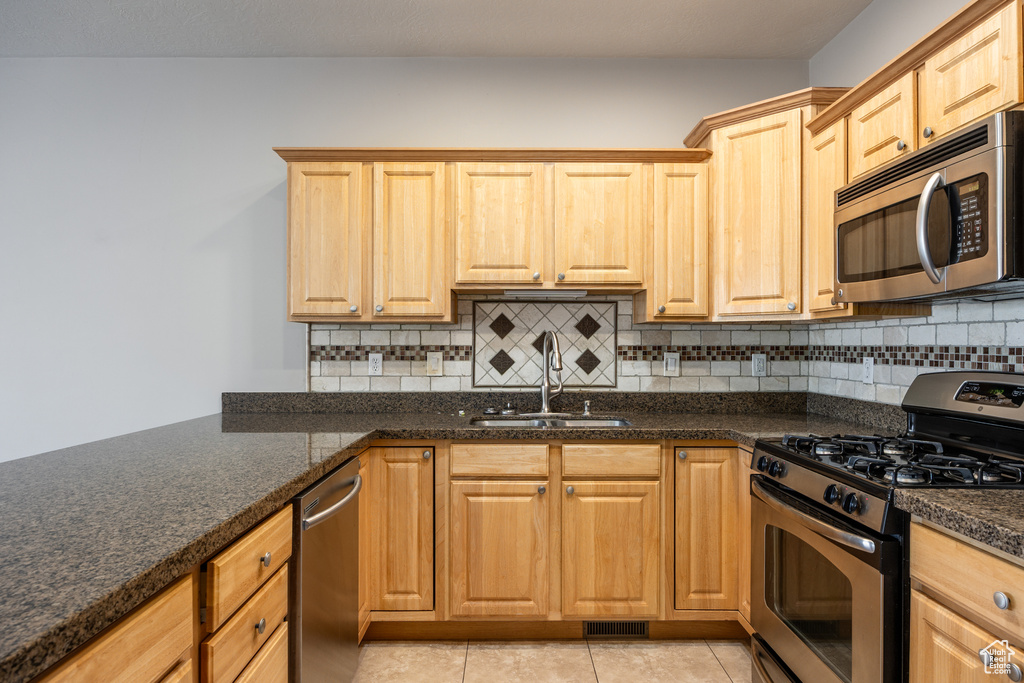 Kitchen featuring a sink, tasteful backsplash, stainless steel appliances, and light tile patterned flooring