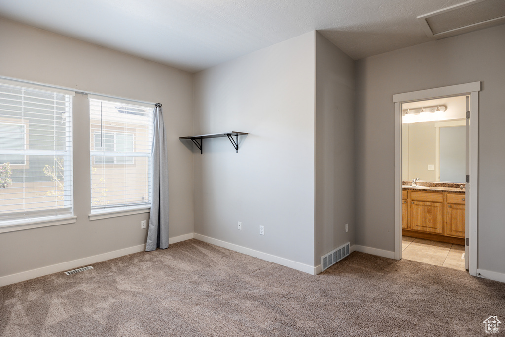 Unfurnished bedroom with light colored carpet, a sink, and visible vents