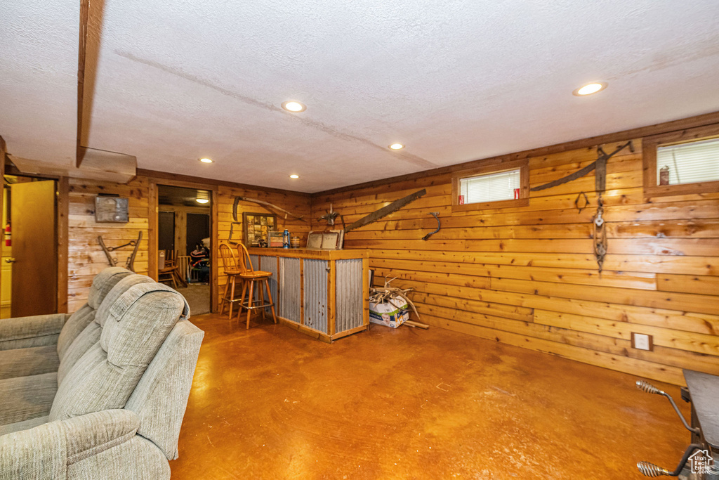 Living room with finished concrete floors, wood walls, a textured ceiling, and recessed lighting