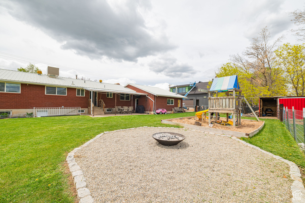 View of yard with fence, central air condition unit, an outdoor fire pit, a playground, and a patio