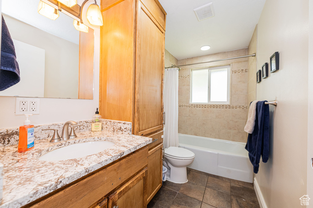 Bathroom featuring stone finish flooring, visible vents, vanity, toilet, and shower / bath combo with shower curtain