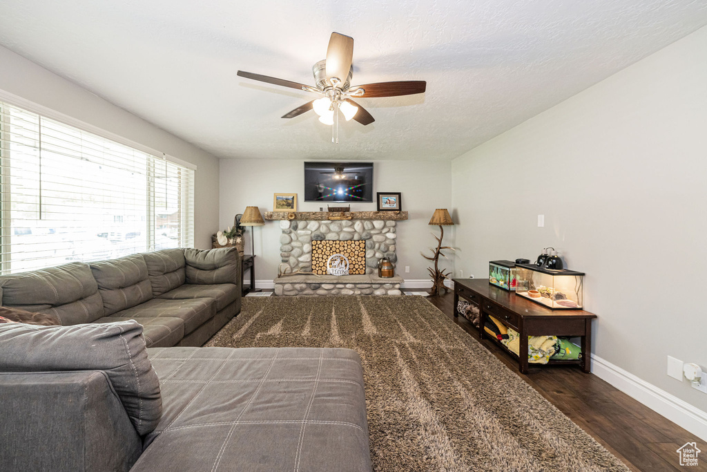 Living area with baseboards, ceiling fan, a stone fireplace, and wood finished floors