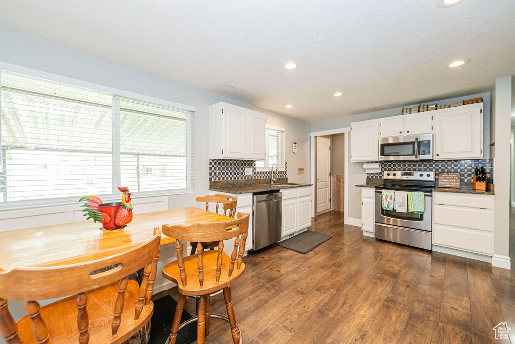 Kitchen featuring backsplash, dark wood-style floors, dark countertops, and stainless steel appliances