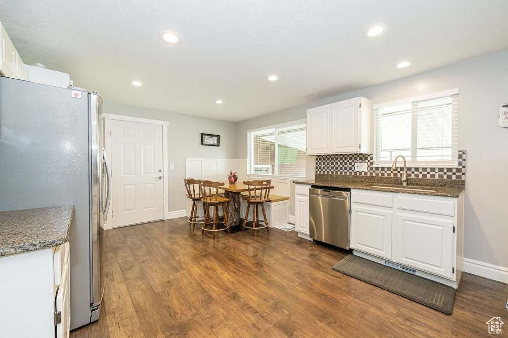 Kitchen featuring appliances with stainless steel finishes, tasteful backsplash, dark wood finished floors, a sink, and white cabinets