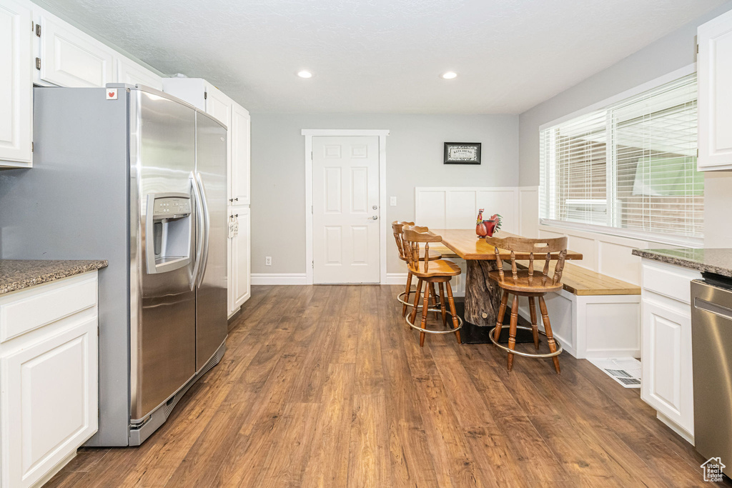 Kitchen featuring dark wood-type flooring, white cabinets, light stone countertops, and stainless steel appliances